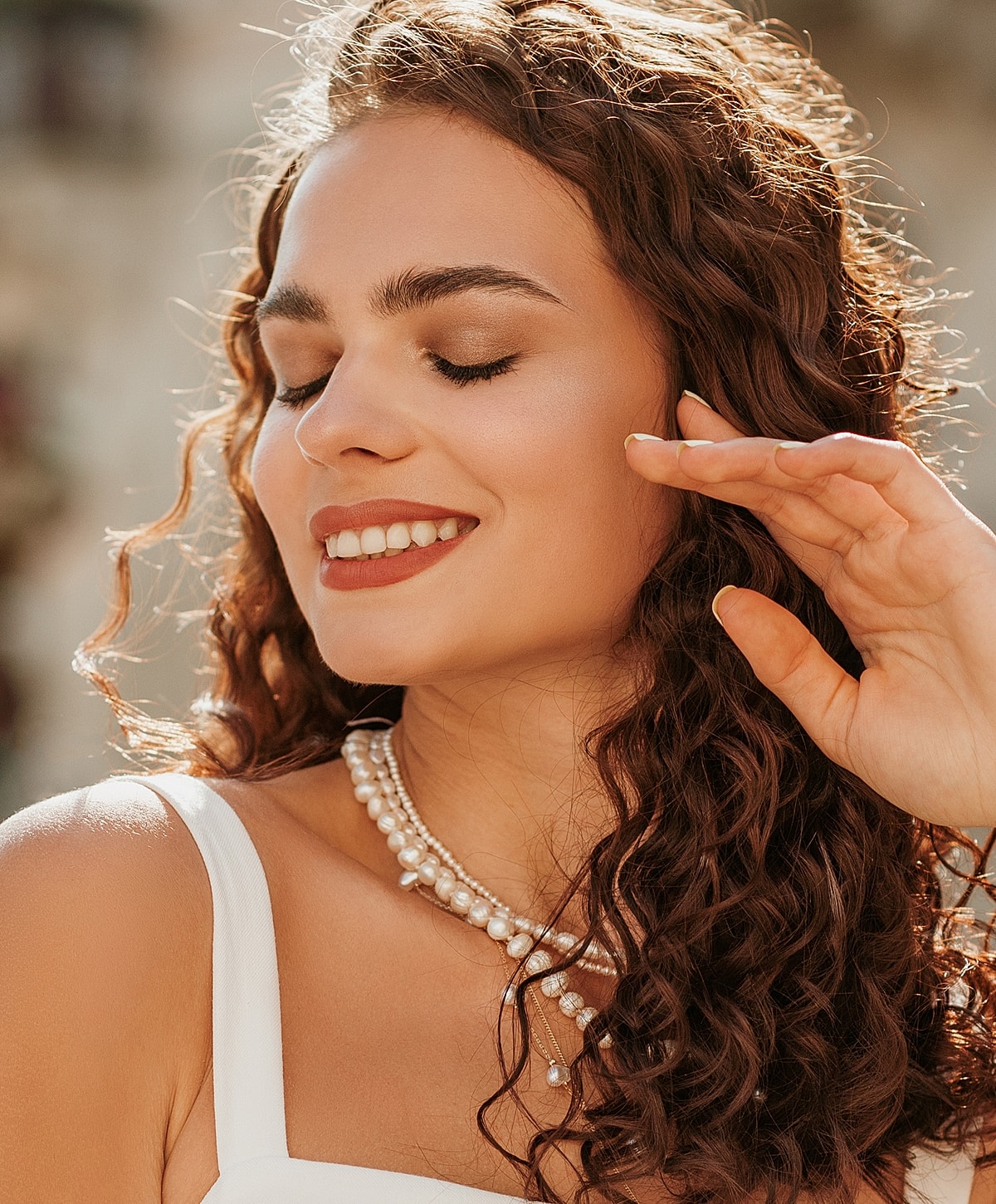 Smiling woman with curly hair and pearl necklace.