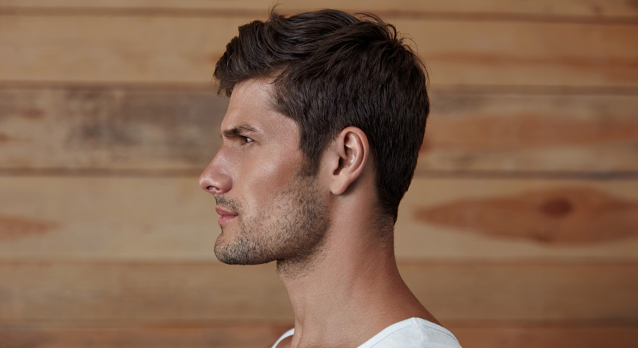 Side profile of a man against a wooden background.