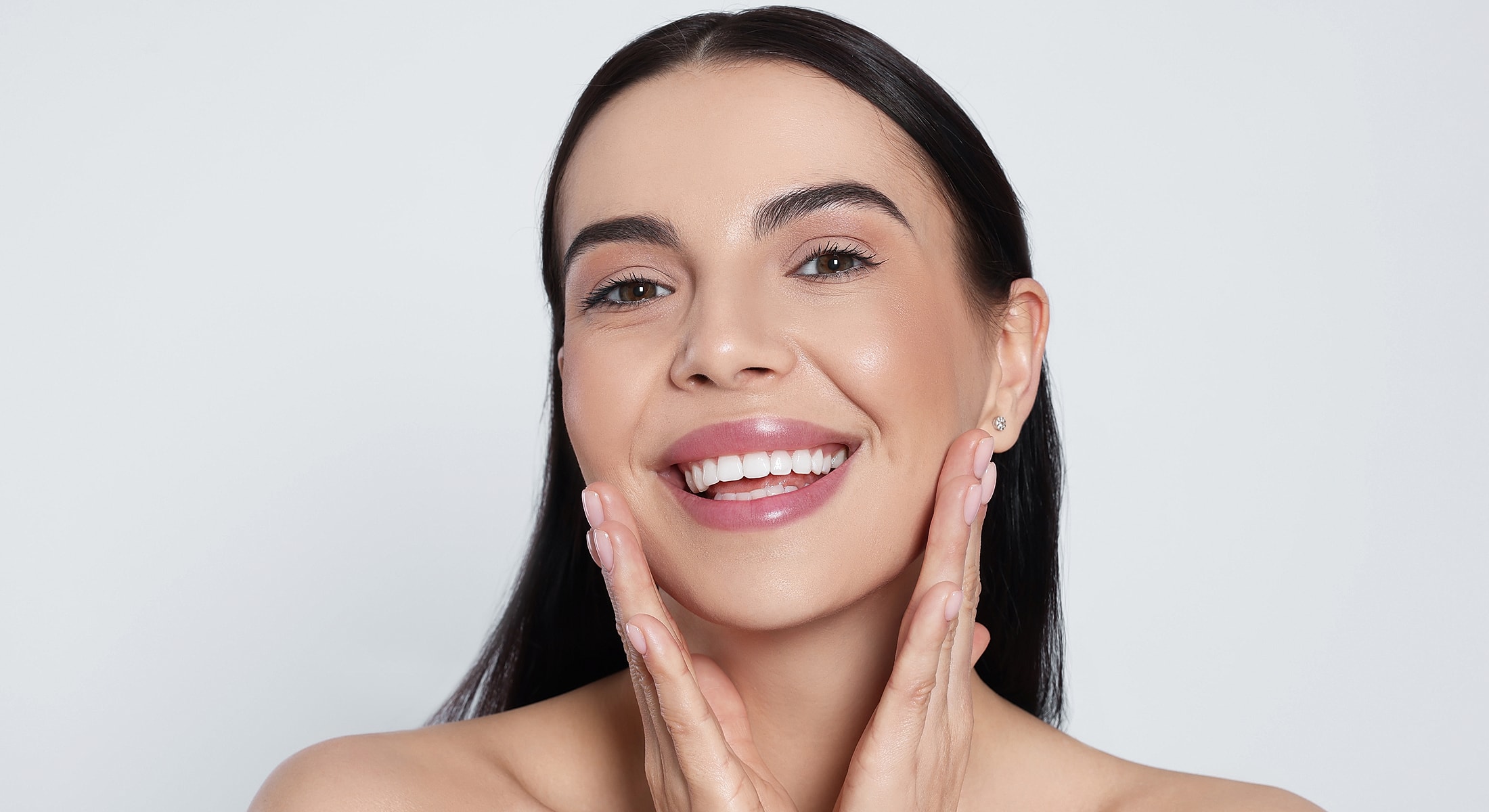 Smiling woman gently touching her face.